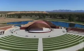 Outdoor amphitheater with a curved stage and seating, surrounded by water and arid landscape.