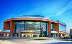 A modern, rounded building with large glass windows and orange exterior walls, illuminated by streetlights under a blue sky.