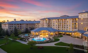 A large hotel complex with blue roofs and illuminated windows, set against a colorful sunset sky.