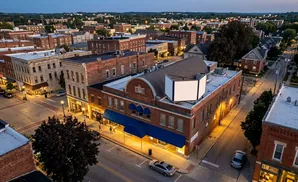 Aerial view of a charming town square with historic brick buildings, streetlights, and a few cars at dusk.