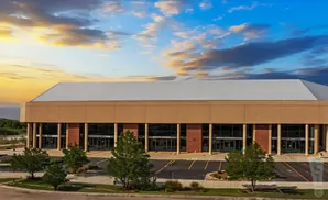 Large tan building with a white roof, glass windows, and trees in front.