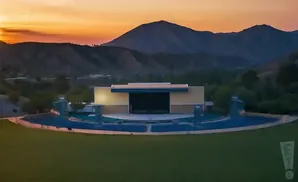 An outdoor amphitheater is illuminated against a sunset with mountains in the background.