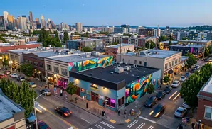 Aerial view of a city street with buildings, cars, and a mural at dusk.