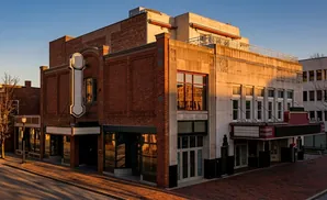 A historic theater with a marquee and large vertical sign sits on a brick street under a clear sky.