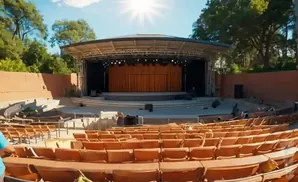 Outdoor amphitheater with rows of empty orange seats facing a stage with a large orange curtain and lights.