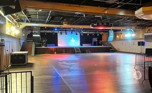 An empty concert venue with a stage, screen, lighting, speakers, and a large open floor.