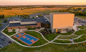 Aerial view of a large building with a basketball court and amphitheater on a sunny day.