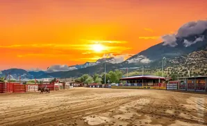 A cowboy rides a horse in a rodeo arena with a mountain backdrop at sunset.
