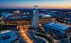 Aerial view of a stadium and surrounding buildings at twilight, with car lights creating streaks on the roads.