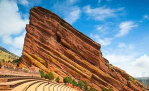 Red Rocks Amphitheatre in Colorado with tiered seating against a massive red rock formation under a blue, cloudy sky.
