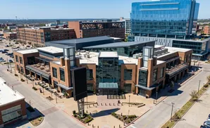 Aerial view of a modern brick building with a glass entrance and a high-rise glass building in the background.