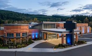 Modern building with orange panels, glass entrance, and blue lights, set against a forested hillside.