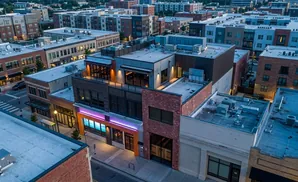 Aerial view of a modern urban street with buildings, shops, and apartments at dusk.