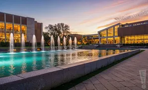 A modern building with large windows and a water fountain at sunset.