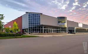 A modern building with large glass windows and a red brick section under a cloudy sky.