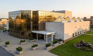 Modern building with reflective gold glass facade and limestone exterior, featuring triangular skylights and a landscaped garden with large sculptures.