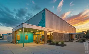 Modern building with teal and metal siding, large windows, and a dramatic sunset sky.