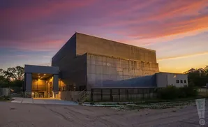 A brutalist concrete building at sunset with a vibrant pink and orange sky.