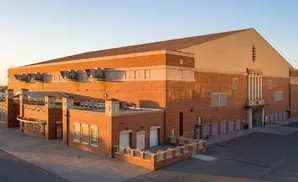 Exterior of a brick building with a large roof, air conditioning units, and a main entrance.