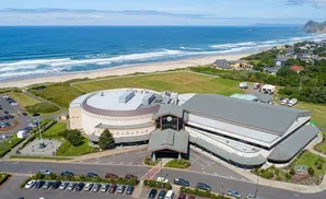 Aerial view of a large casino and hotel complex on the Oregon coast, with the Pacific Ocean and beach in the background.