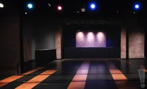 A dimly lit stage with brick backdrop and purple spotlights.