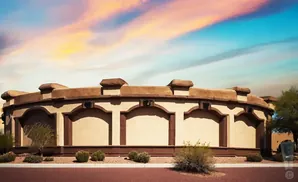 A curved, stucco building with decorative arches and battlements against a colorful sky.