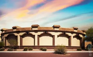 A curved, tan building with arched recesses and decorative top against a colorful sky.