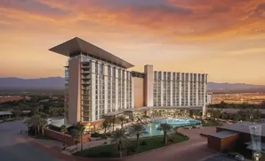 Modern hotel with a large pool and palm trees at sunset.