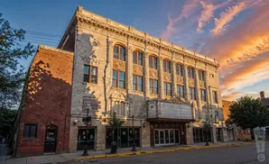 An ornate stone theater building with a brick addition, bathed in the warm glow of a sunset.