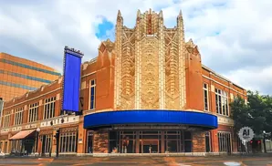 Art deco theater with ornate facade, brick building, blue awning, and a tall blue banner.