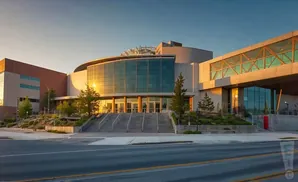 Modern building with a curved glass facade and a skybridge, bathed in warm evening light.