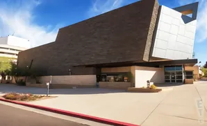 Modern building with dark stone and white metal facade under a blue sky with clouds.