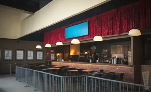 Interior of a bar with a long counter, tables, and a large red curtain hanging above a flat-screen TV.