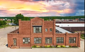 Drone view of a brick building with a broken roof under a dramatic sunset sky.