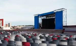 An outdoor amphitheater with a stage, seating, and a city skyline in the background.