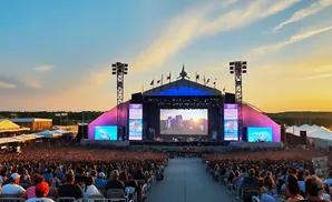 Outdoor concert at sunset with a large crowd and a massive stage with screens displaying a castle.