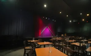 A comedy club stage with red curtains and tables with chairs in the foreground.