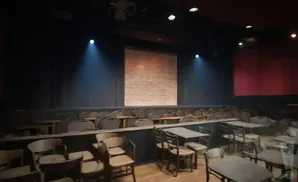 An empty theater with stage, brick backdrop, and rows of chairs and tables.