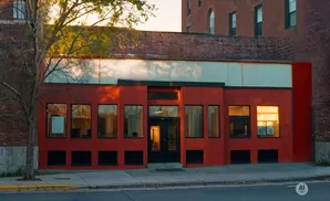 A red building with large windows and a tree in front.
