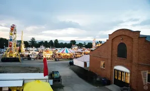 A fairground with rides, tents, and a brick building under a cloudy sky.