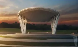 An outdoor amphitheater with a white, modern roof supported by sculptural pillars, set against a sunset sky.