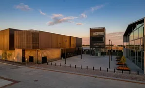 Modern buildings with metal facades and glass windows at sunset, featuring an outdoor plaza with benches and trees.