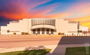 Modern beige building with a large arched glass entrance against a vibrant sunset sky.