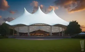 Outdoor amphitheater with a large white tent structure and a backdrop of a colorful sunset sky.