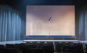 A stage with a microphone and a blank screen, with an audience in the foreground.