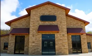 A modern stone building with a red roof and large glass doors, under a blue sky with clouds.