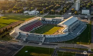 Aerial view of a large stadium with red and blue seats, a green field, and a covered seating area.