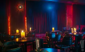 A dimly lit room with red and blue stage lights, dark curtains, and tables set with candles.