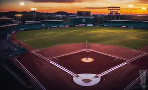 Aerial view of a baseball field at sunset, with lights on and players on the field.