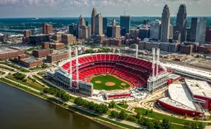 Aerial view of a baseball stadium with red seats, a green field, and a city skyline in the background.
